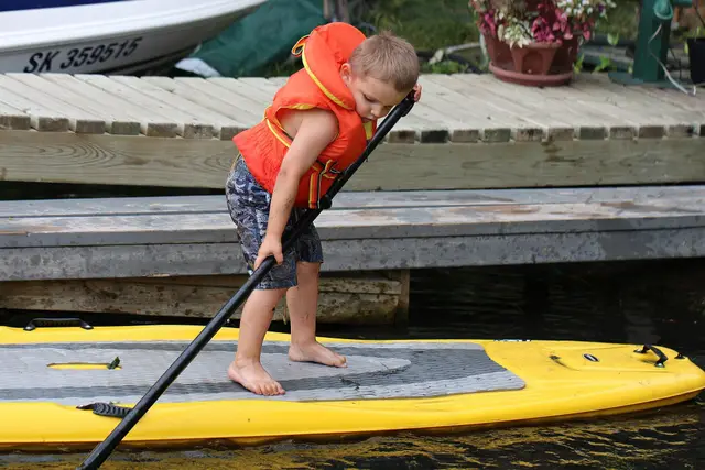 Child paddle boarding beside a dock